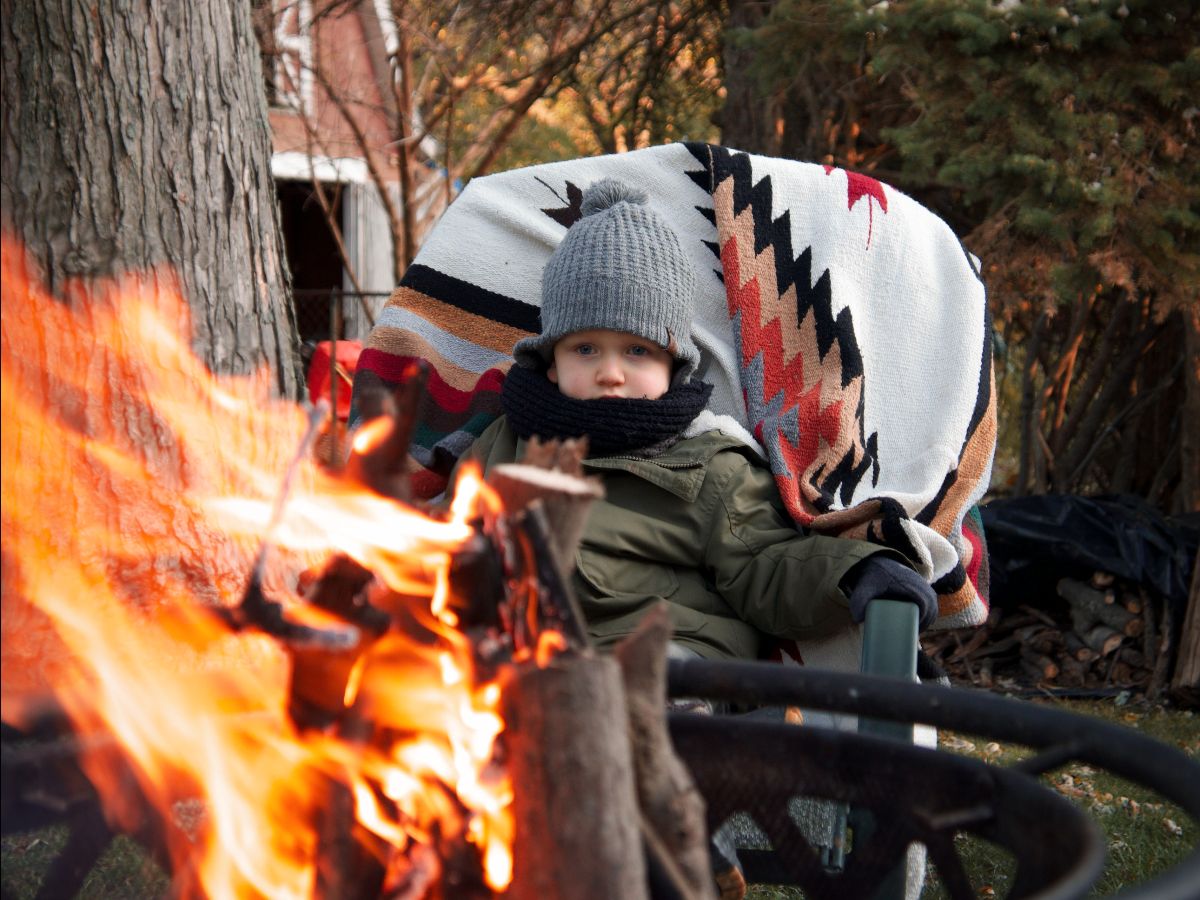 Small boy sits in chair in front of fire- ways to make leaf raking fun