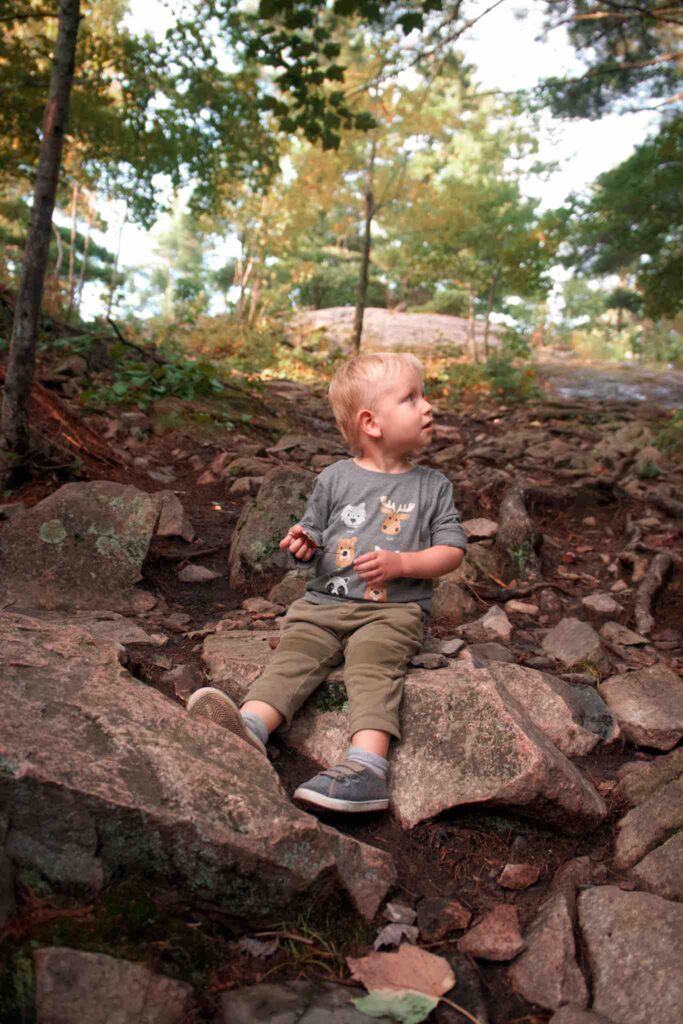 While hiking with toddler, small boy stops to sit on some large rocks in middle of trail. 