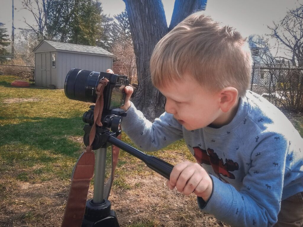 Outdoor Creative arts ideas for kids: Small boy with camera on tripod taking pictures in his backyard. 