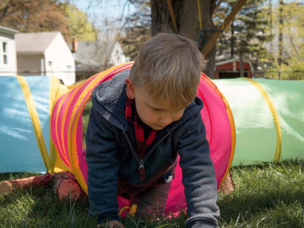 small boy crawling through a play fabric tunnel-essential backyard toys