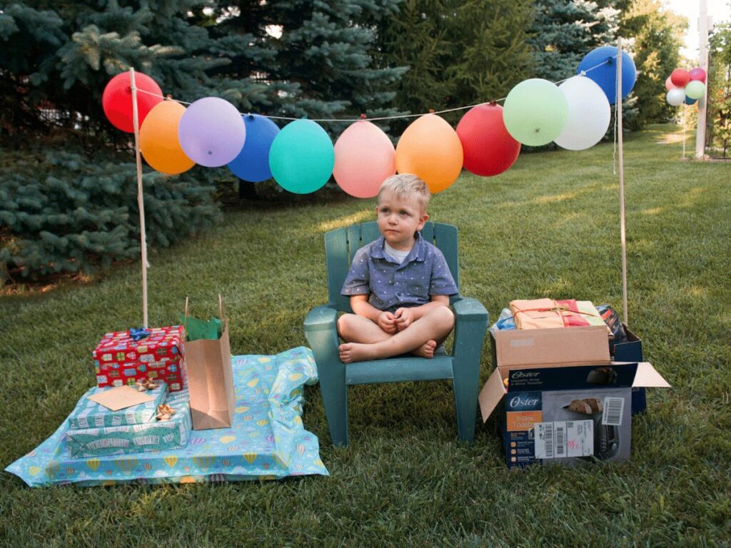 small boy sits on chair outside surrounded by balloons and presents- summer bucket list