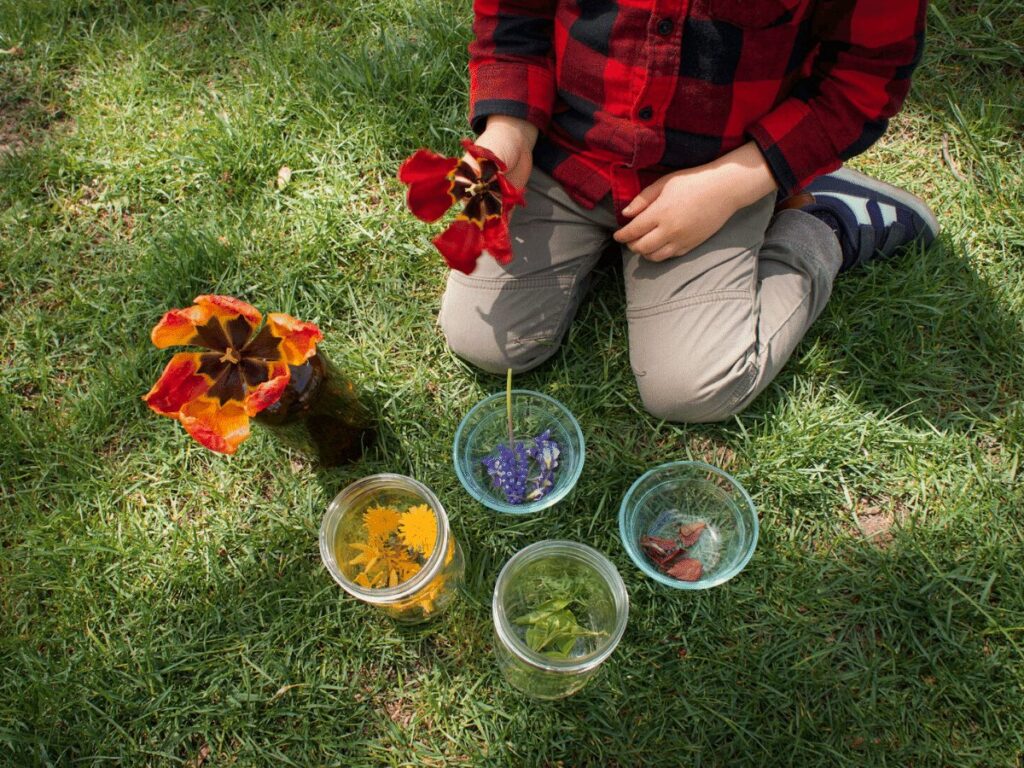 Small boy surrounded by jars  of different colored nature pieces for rainbow craft. 