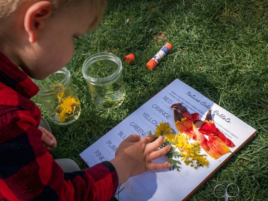 Small boy glues variety of colorful nature pieces onto paper for rainbow craft. 