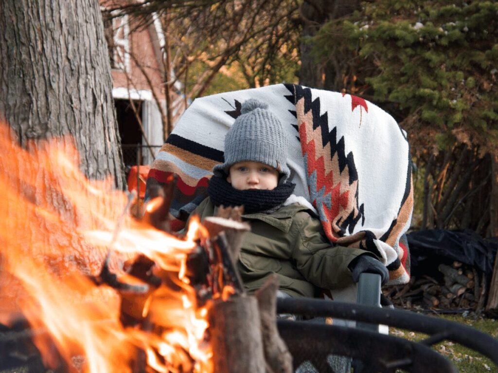 small boy sitting by fire- best outdoor toys