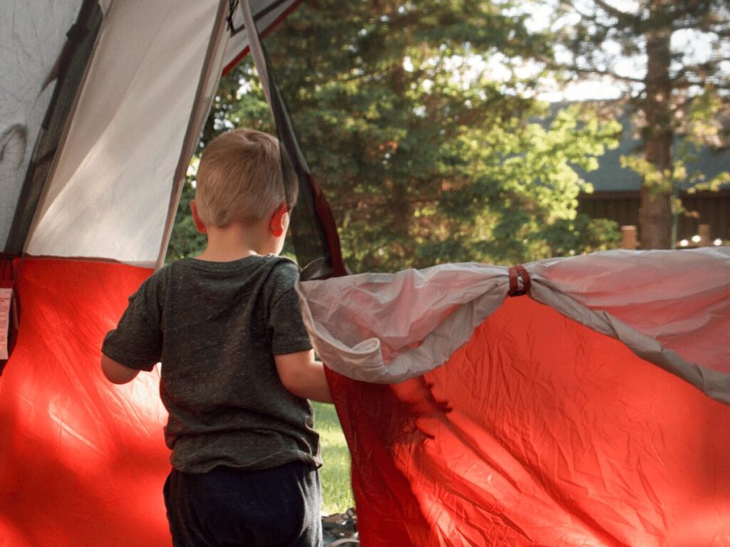 Summer bucket list- small boy opening doorway of tent while camping out