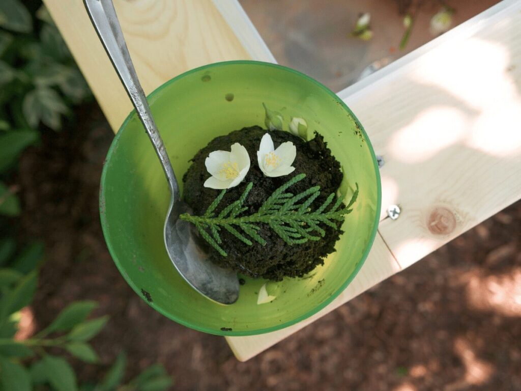 mud "ice cream" in a bowl with flower and cedar garnish on mud kitchen counter