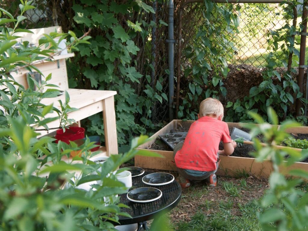 small boy plays in mud kitchen area outside