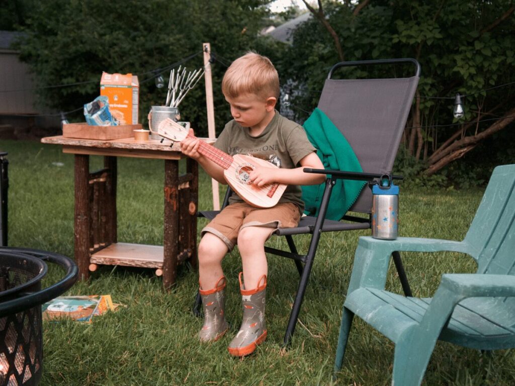small boy strums guitar in front of campfire