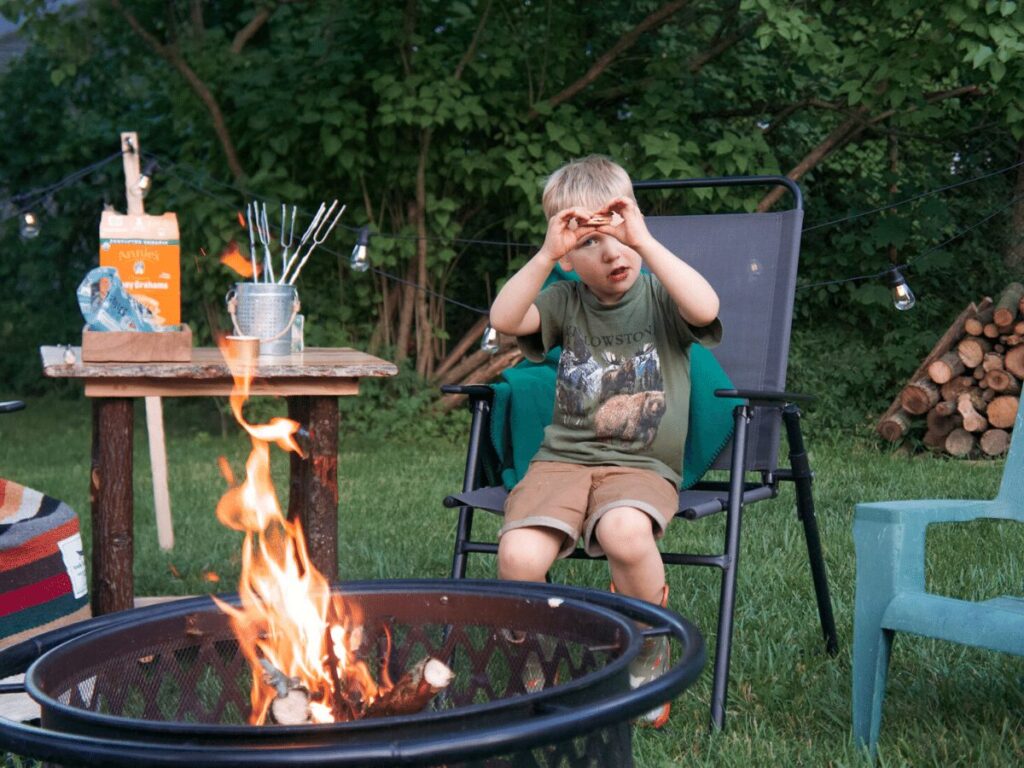 small boy sits in front of campfire holding s'more.