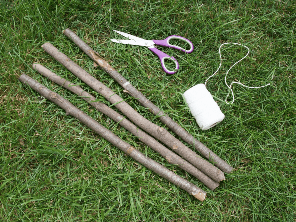 materials needed for a nature weaving- four sticks, scissors, and a roll of string spread out on the grass