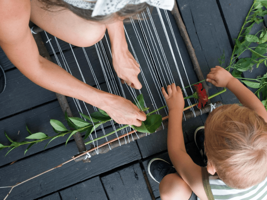 Overhead shot of mom and small boy weaving plants into loom to make a nature weaving