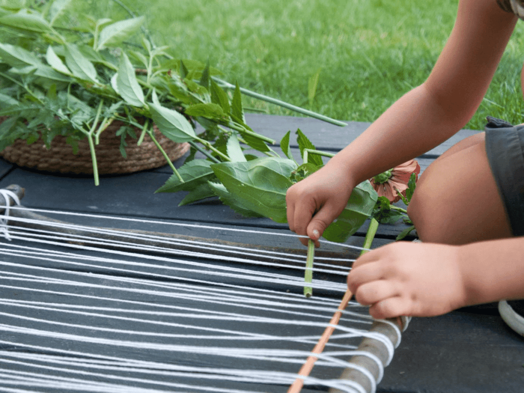 Close up of small boy's hands weaving plants into loom for nature weaving