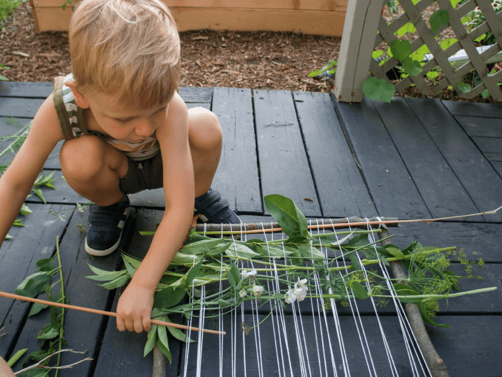 small boy adding more plants to his nature weaving loom