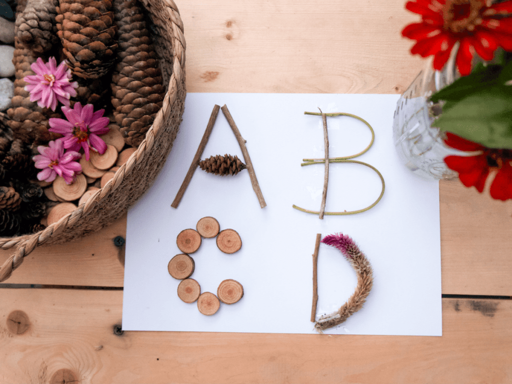 preschool activities, letters a, b, c, and d created on a piece of paper using twigs, pine cones, and wood slices.