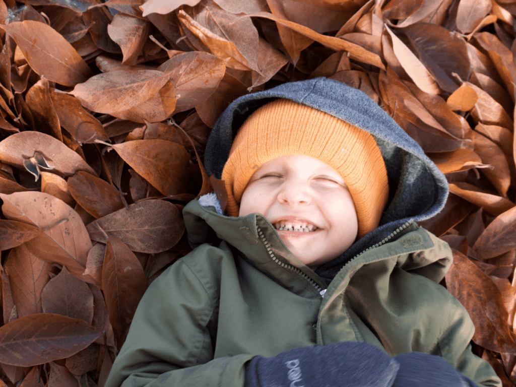 fall bucket list, small boy laying in pile of leaves and laughing