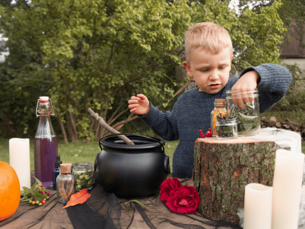 halloween activities for kids, young boy at table with cauldron and bottles of ingredients for potion mixing
