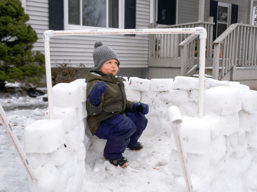 small boy sitting in snow fort