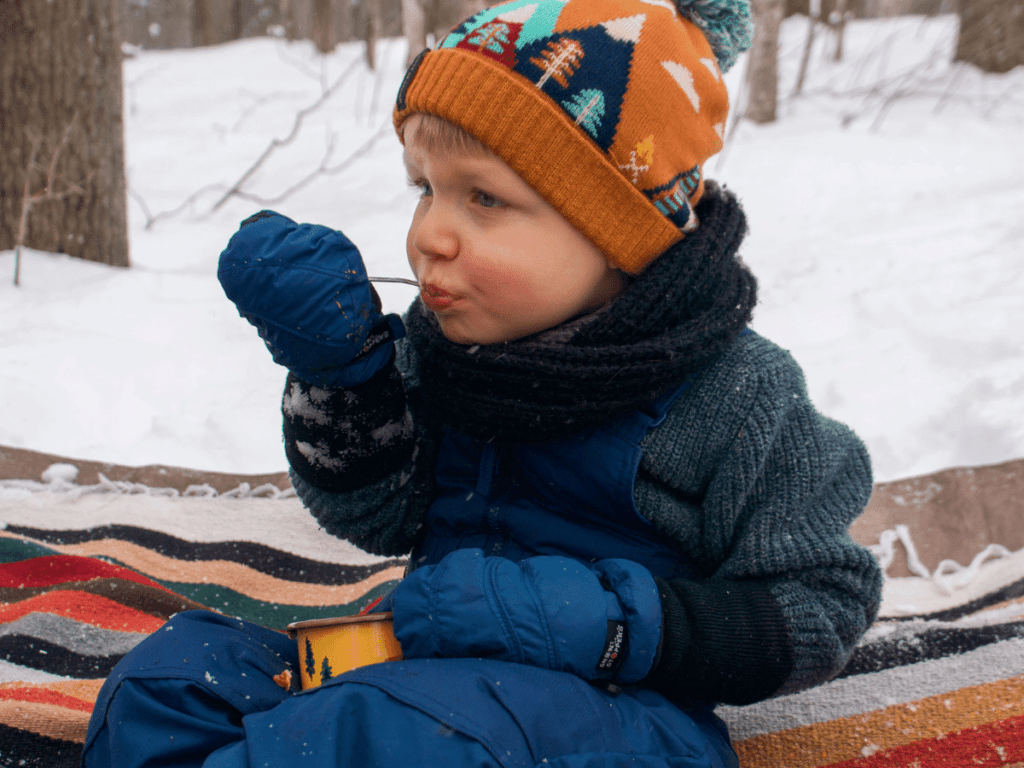 small boy eating chili outside on blanket