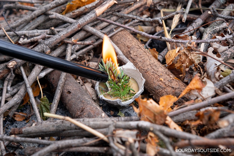 fire starter being lit on a pile of twigs and leaves