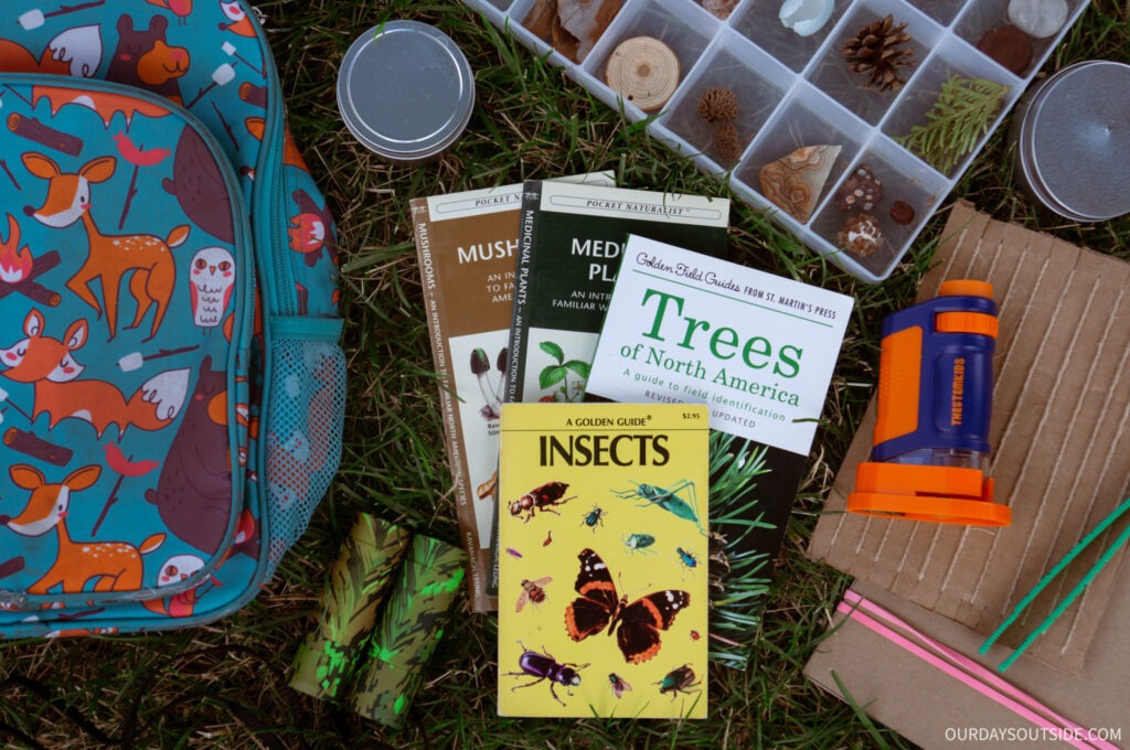 Collection of items spread out on the ground to make a nature explorer kit, including backpacks, field guides, mini microscope, etc. 