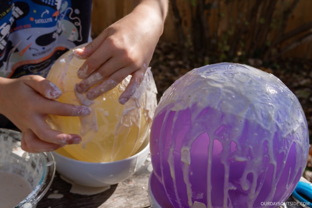 hands of child putting paper mache layers over a balloon to make paper mache lanterns