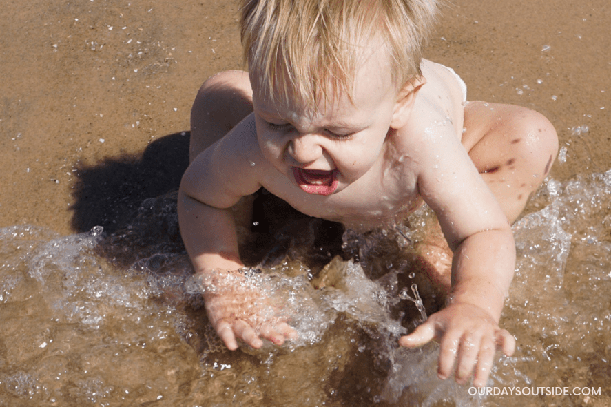 beach packing list for babies and toddlers - toddler boy splashing in the water at the beach