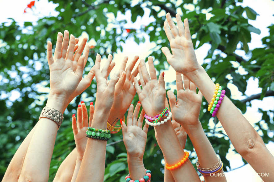 summer camp crafts - a bunch of hands up in the air showing off multiple colored bracelets