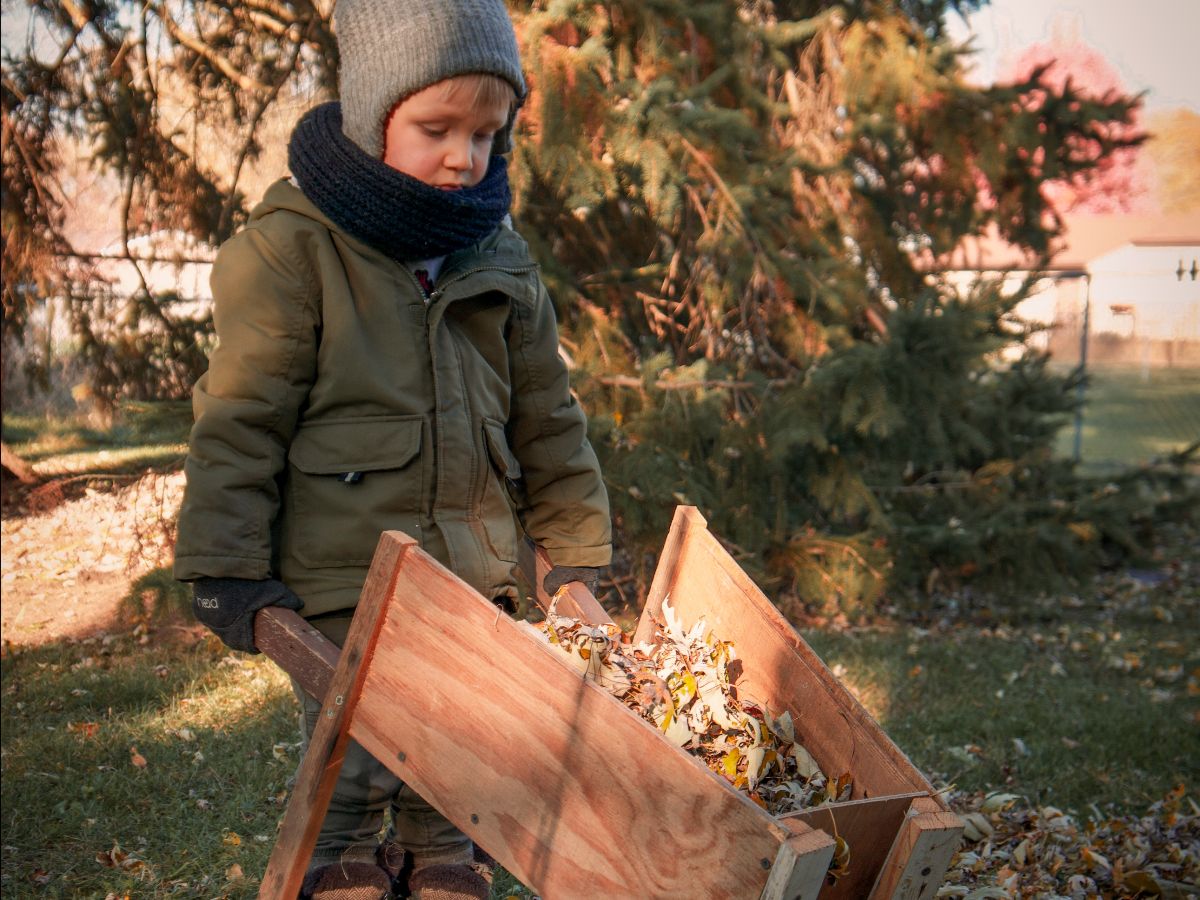 Small boy pushes leaves in wheelbarrow- ways to make leaf raking fun