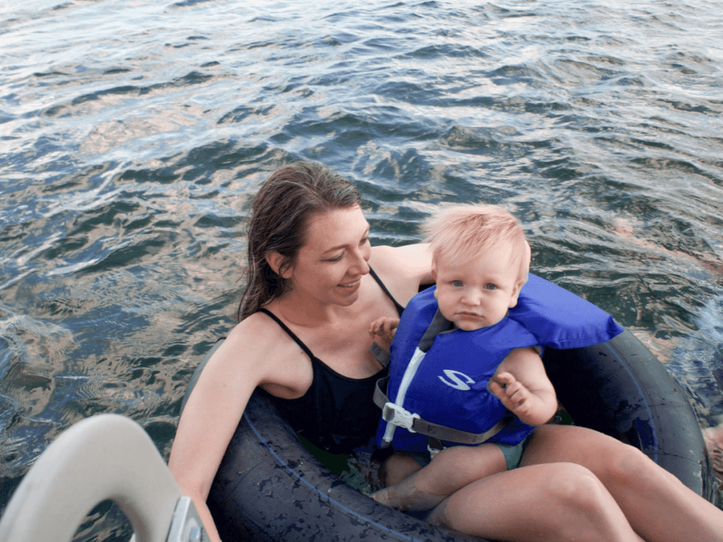 small boy wearing life jacket sits on mom's lap on tube floating in water- outdoor gear for babies