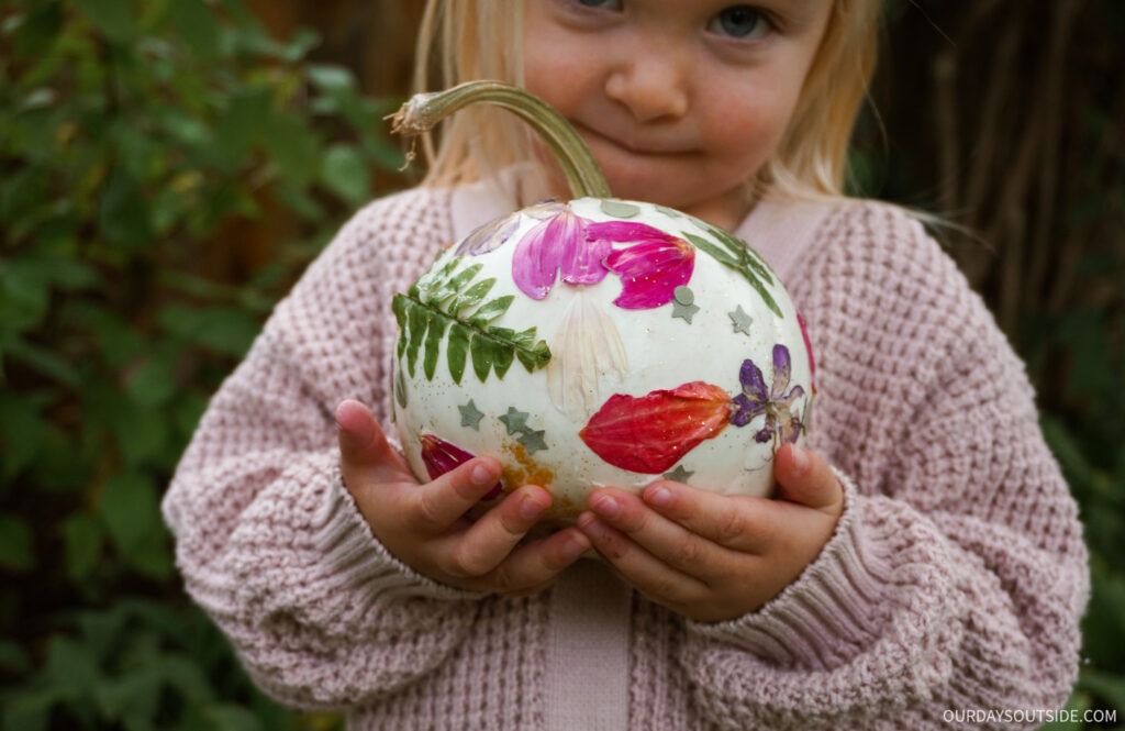 small girl holding a pumpkin decorated with flower petals, ferns, and confetti - no carve pumpkin ideas