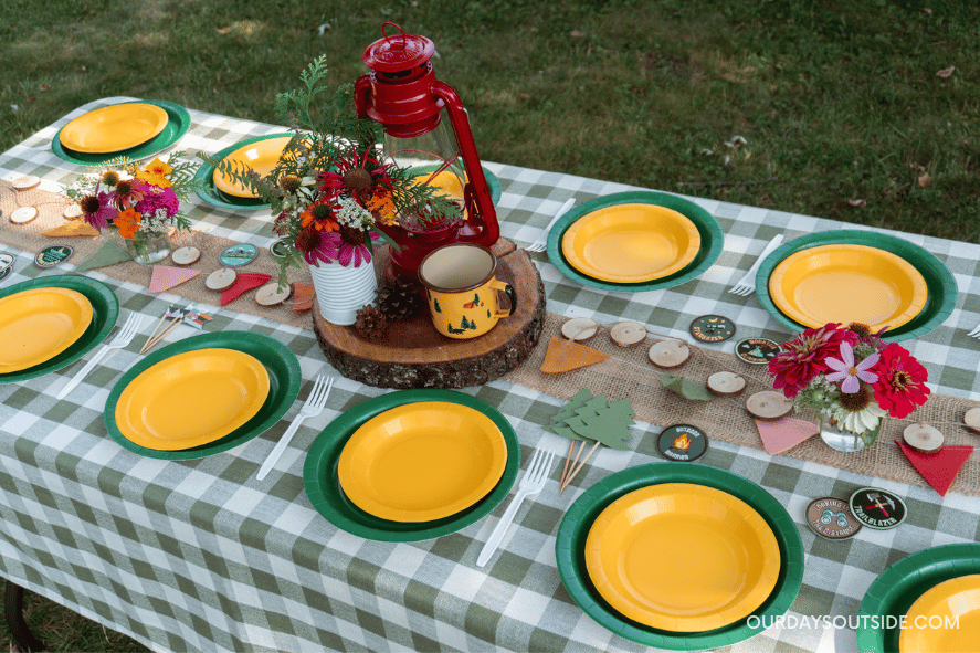 camp birthday party - table shown with green gingham tablecloth, green and white party plates, and lanterns, camp cups, and patches